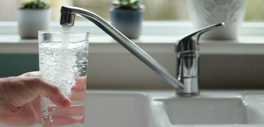 Water flowing from kitchen tap into drinking glass.