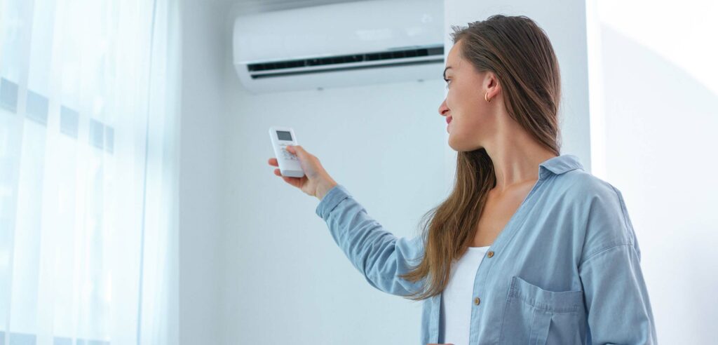 Woman using remote control to adjust indoor temperature.