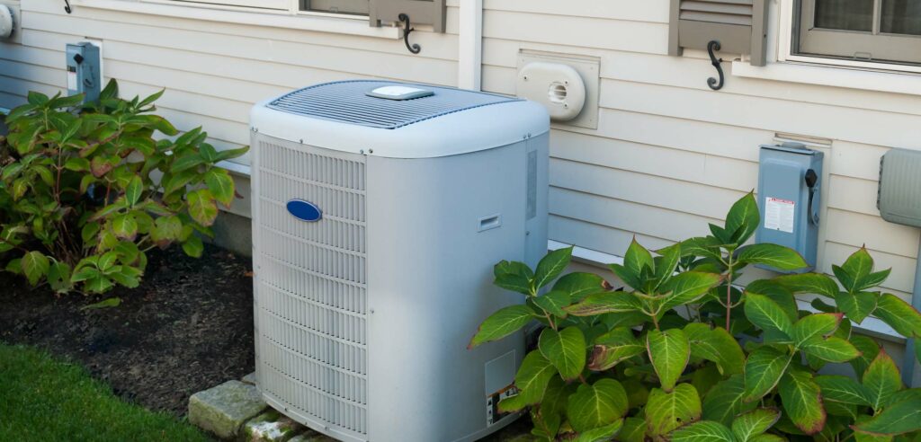 AC Unit outside home with healthy plants beside it.