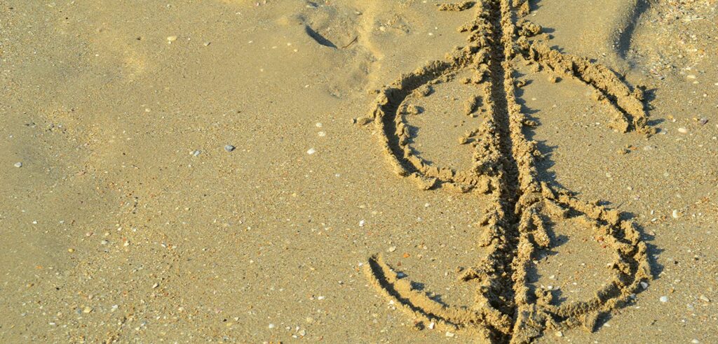 Dollar sign drawn into sand on beach.