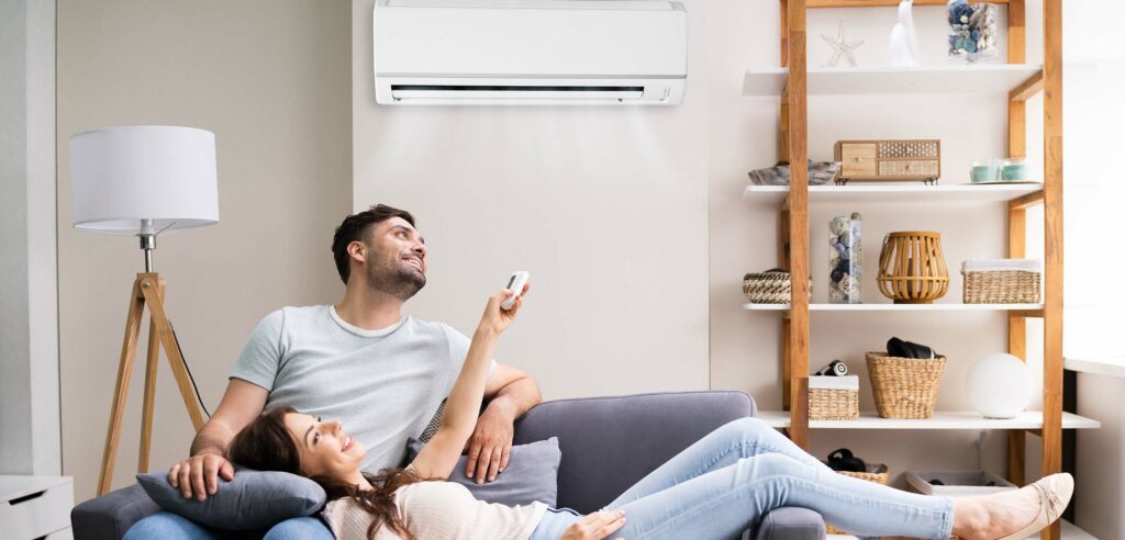 Young couple laying on couch, adjusting indoor temperature with remote control.