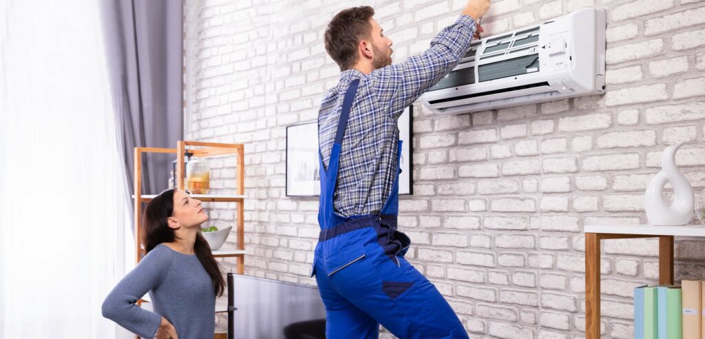 Worker installing ventilation inside home while homeowner watches.