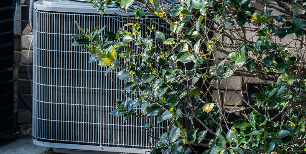 AC unit partially covered by shrubs,outside home