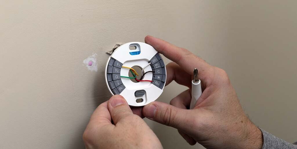 Technician installing smart thermostat on wall in home.