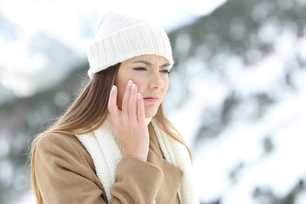 Angry woman using a sking protection moisturizer cream in winter in a snowy mountain