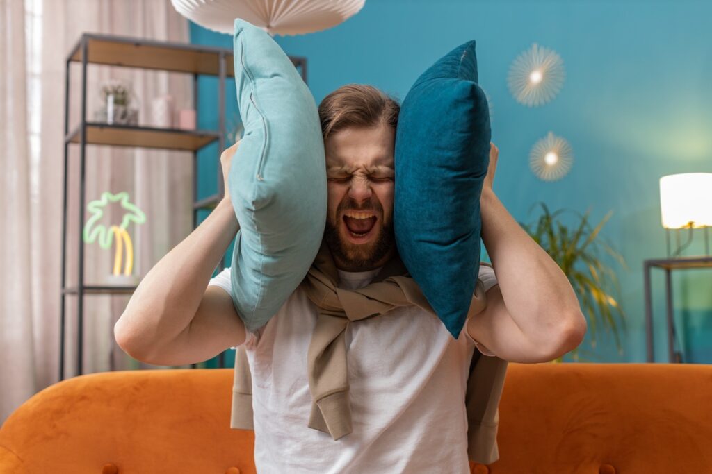 Homeowner holding pillows over ears to drown out AC noise