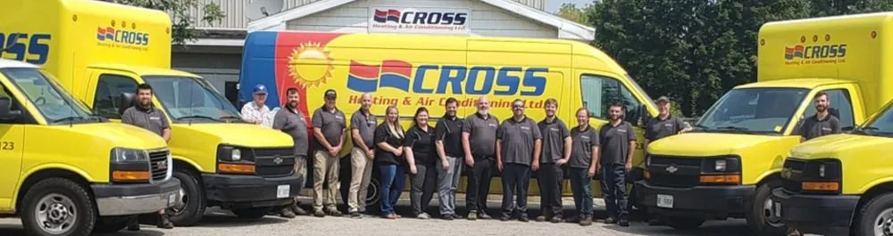 The Cross Heating team standing in front of their building with their yellow trucks and vans surrounding them.
